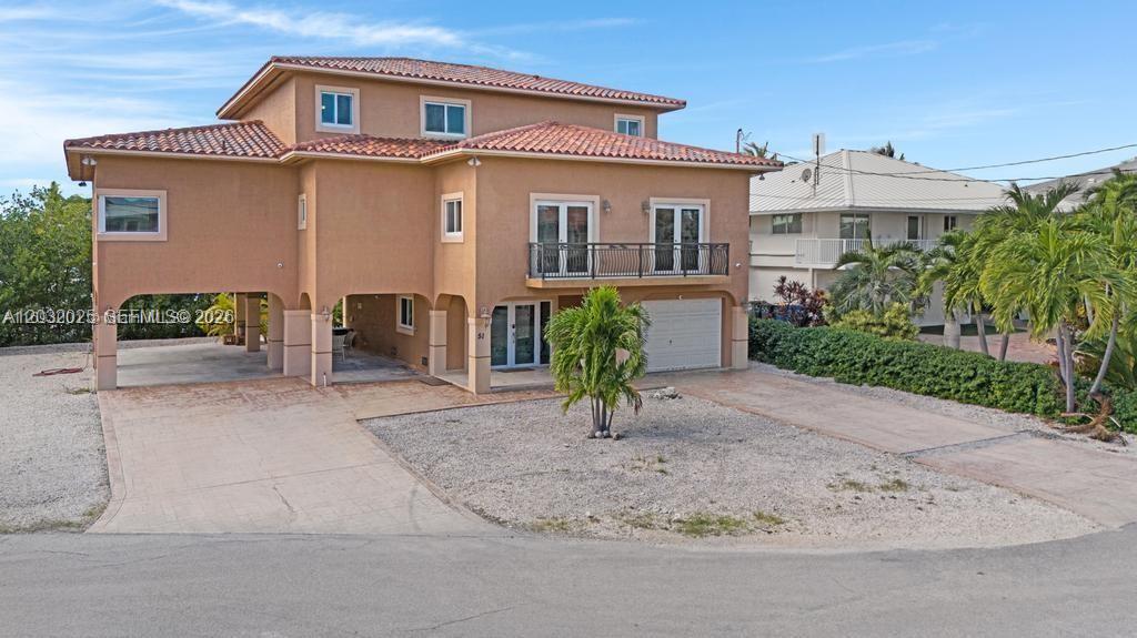 A two-story house with a tan stucco exterior, a tiled roof, and a gravel driveway — 51 W Plaza Del Lago, Islamorada FL 33036, ISLAMORADA, FL