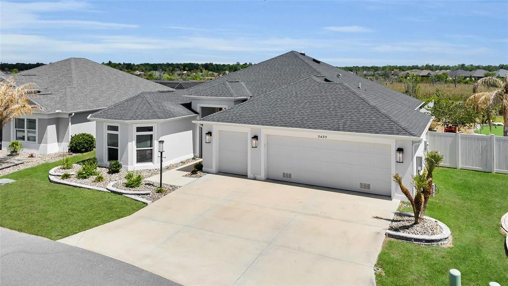A single-story house with a gray shingled roof, white stucco exterior, and a three-car garage — 5495 HAWKINS DRIVE, THE VILLAGES, FL