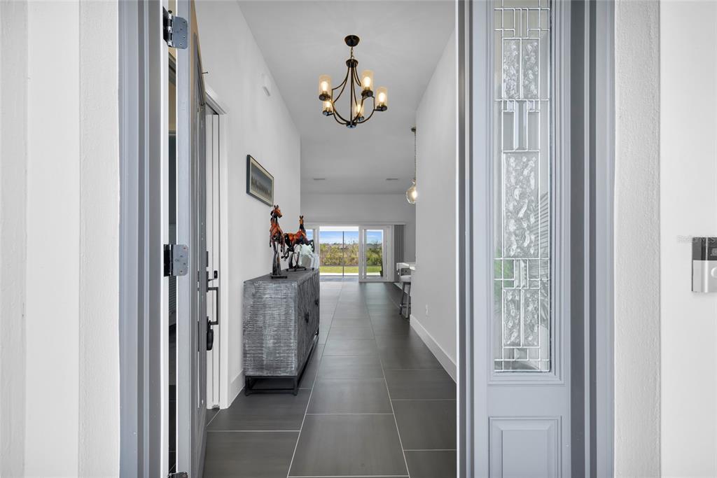 A covered entryway features a gray front door with glass panels, a hanging lantern, and landscaping — 5495 HAWKINS DRIVE, THE VILLAGES, FL