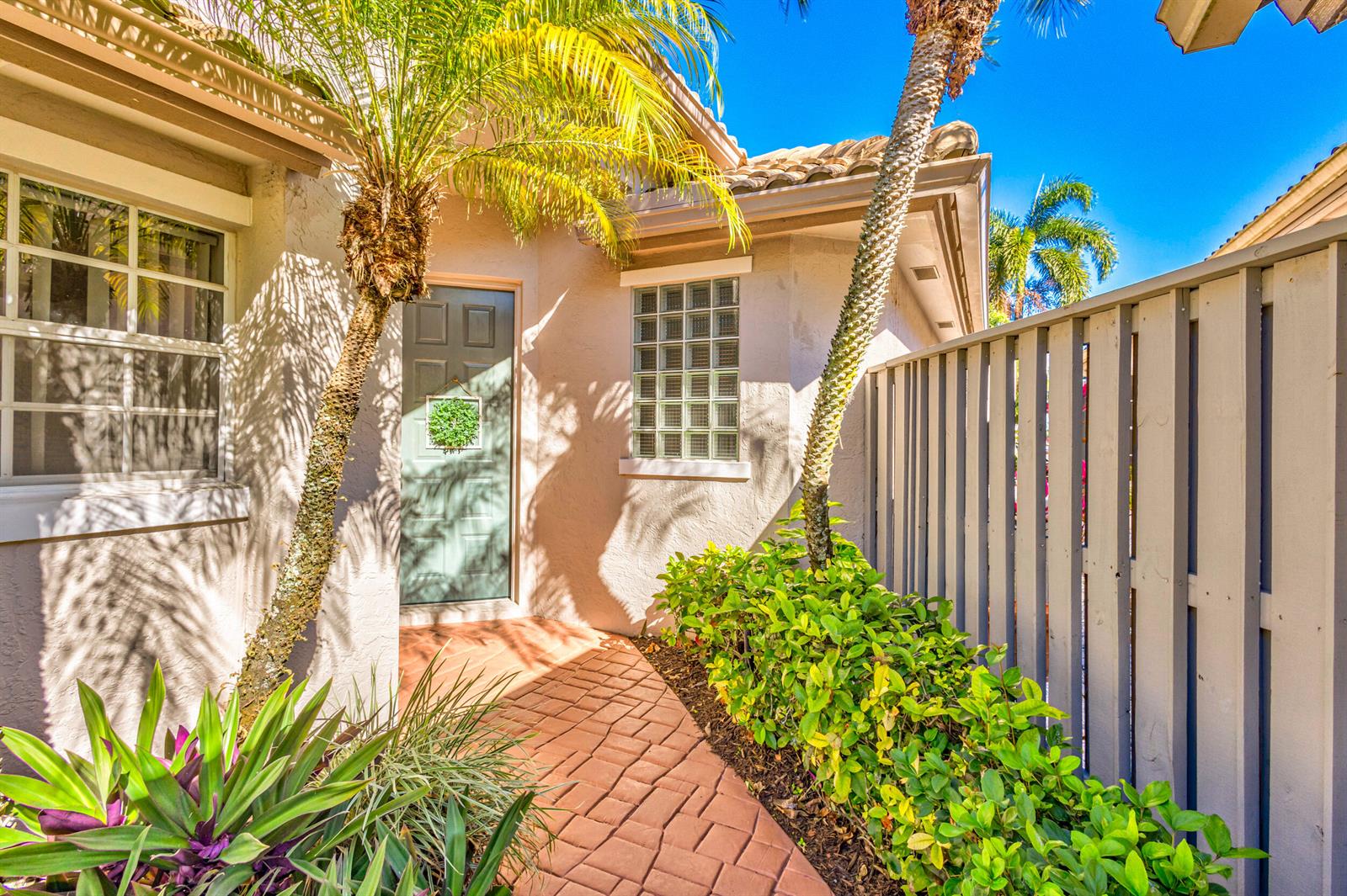 A paved walkway leads to a front door with a glass block window nearby — 919 Augusta Pointe Drive, Palm Beach Gardens FL 33418, PALM BEACH GARDENS, FL