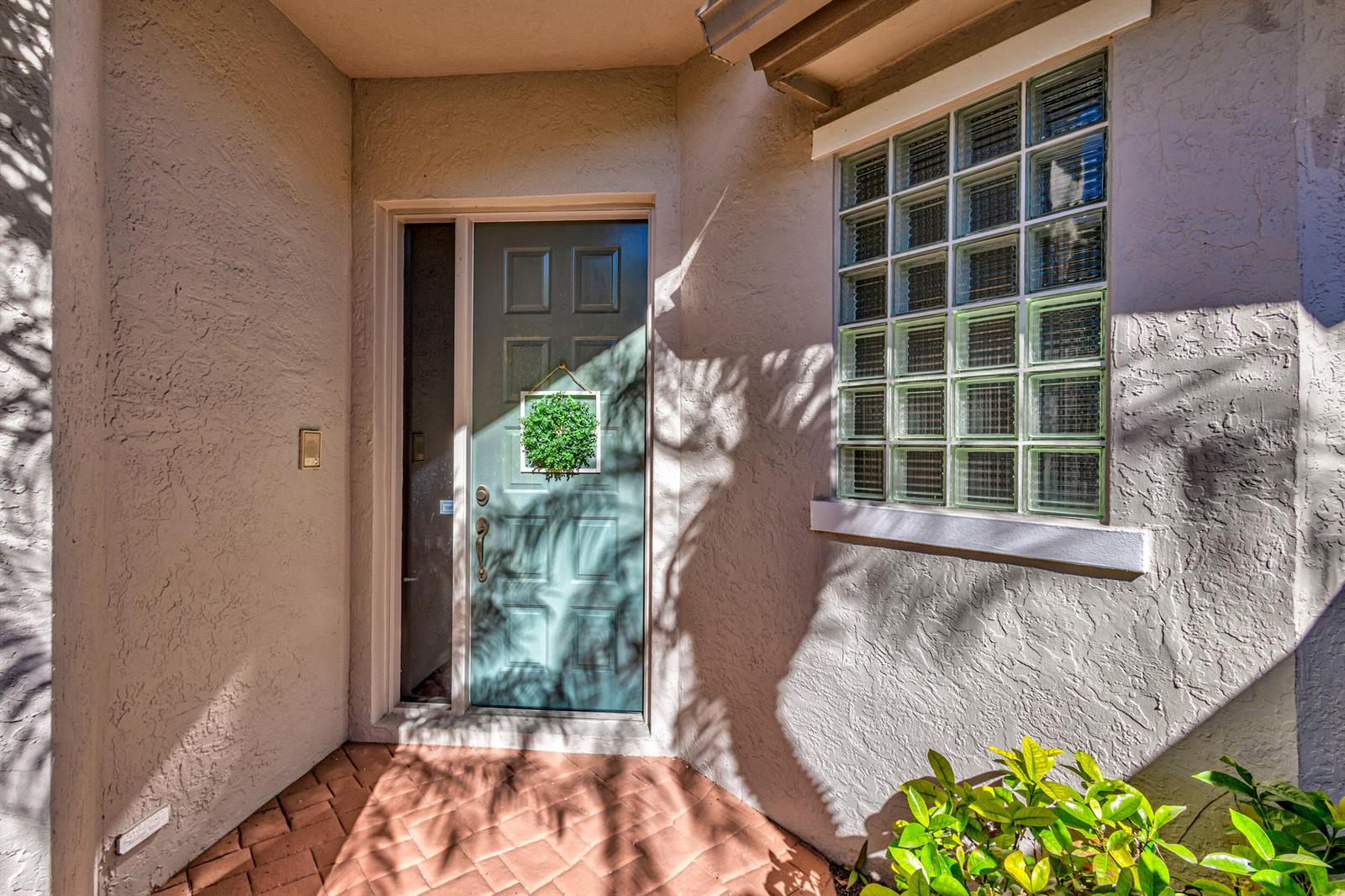 A teal front door with a green wreath sits beside a glass block window — 919 Augusta Pointe Drive, Palm Beach Gardens FL 33418, PALM BEACH GARDENS, FL