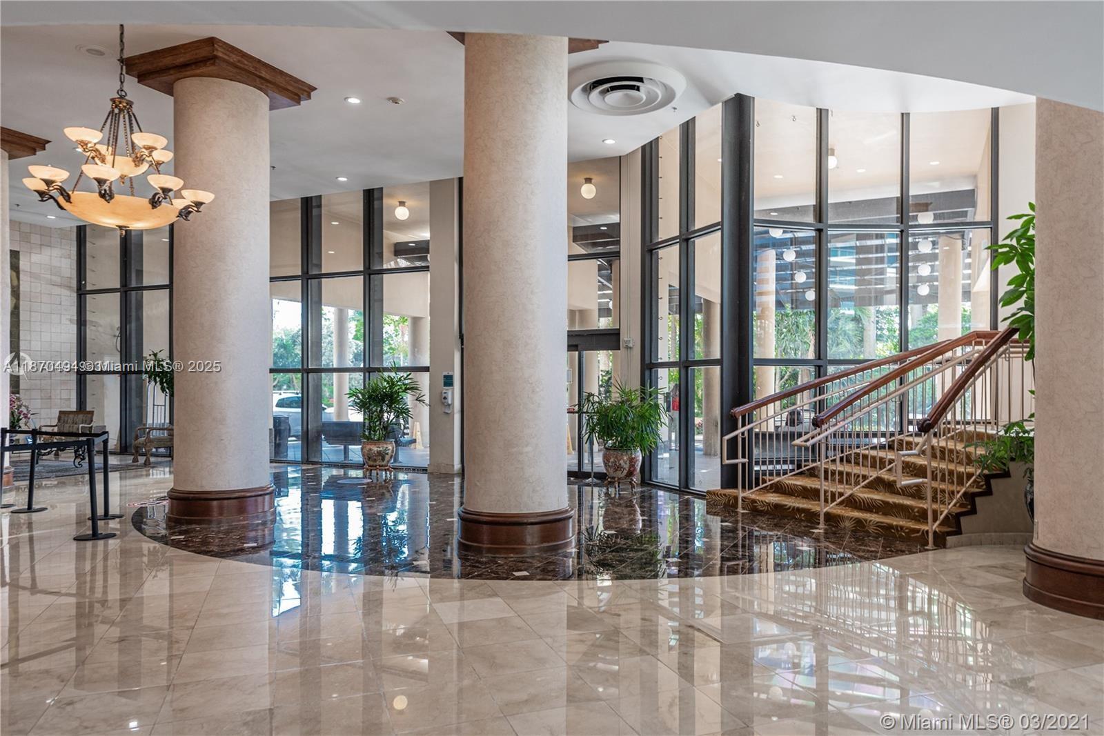 A lobby features large columns, marble floors, a chandelier, and a staircase with metal railings — 10185 Collins Ave # 319, Bal Harbour FL 33154, BAL HARBOUR, FL