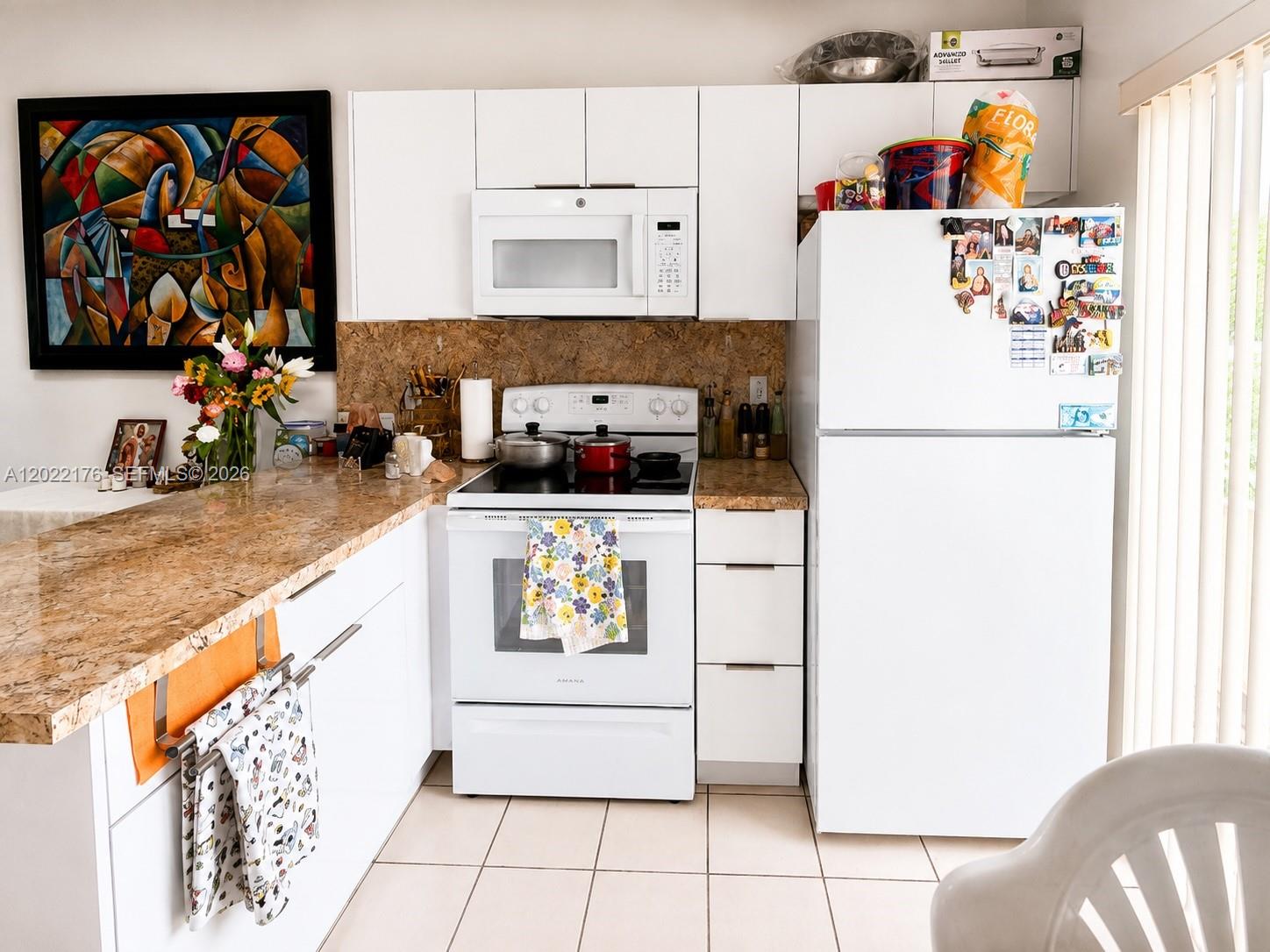 A kitchen features white cabinets, white appliances, a granite countertop, and a colorful abstract painting — 7603 W 29th Ln # 55, Hialeah FL 33018, HIALEAH, FL