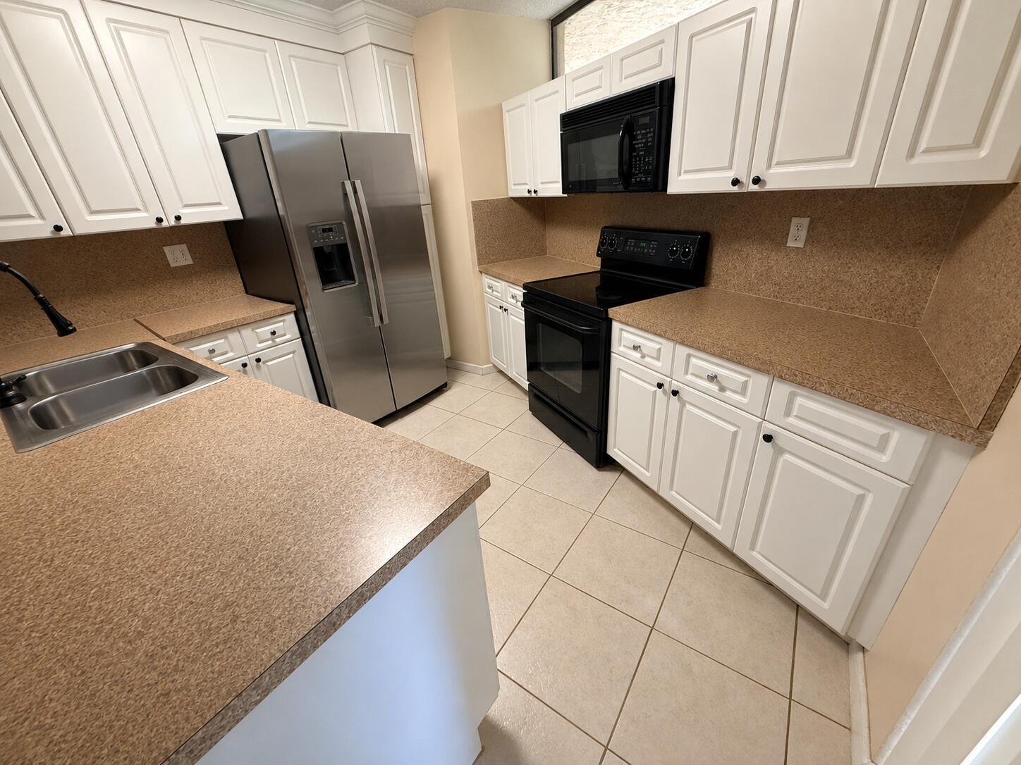 A kitchen features white cabinets, tan countertops, stainless steel refrigerator, and black appliances — 8255 Severn Drive # D, Boca Raton FL 33433, BOCA RATON, FL