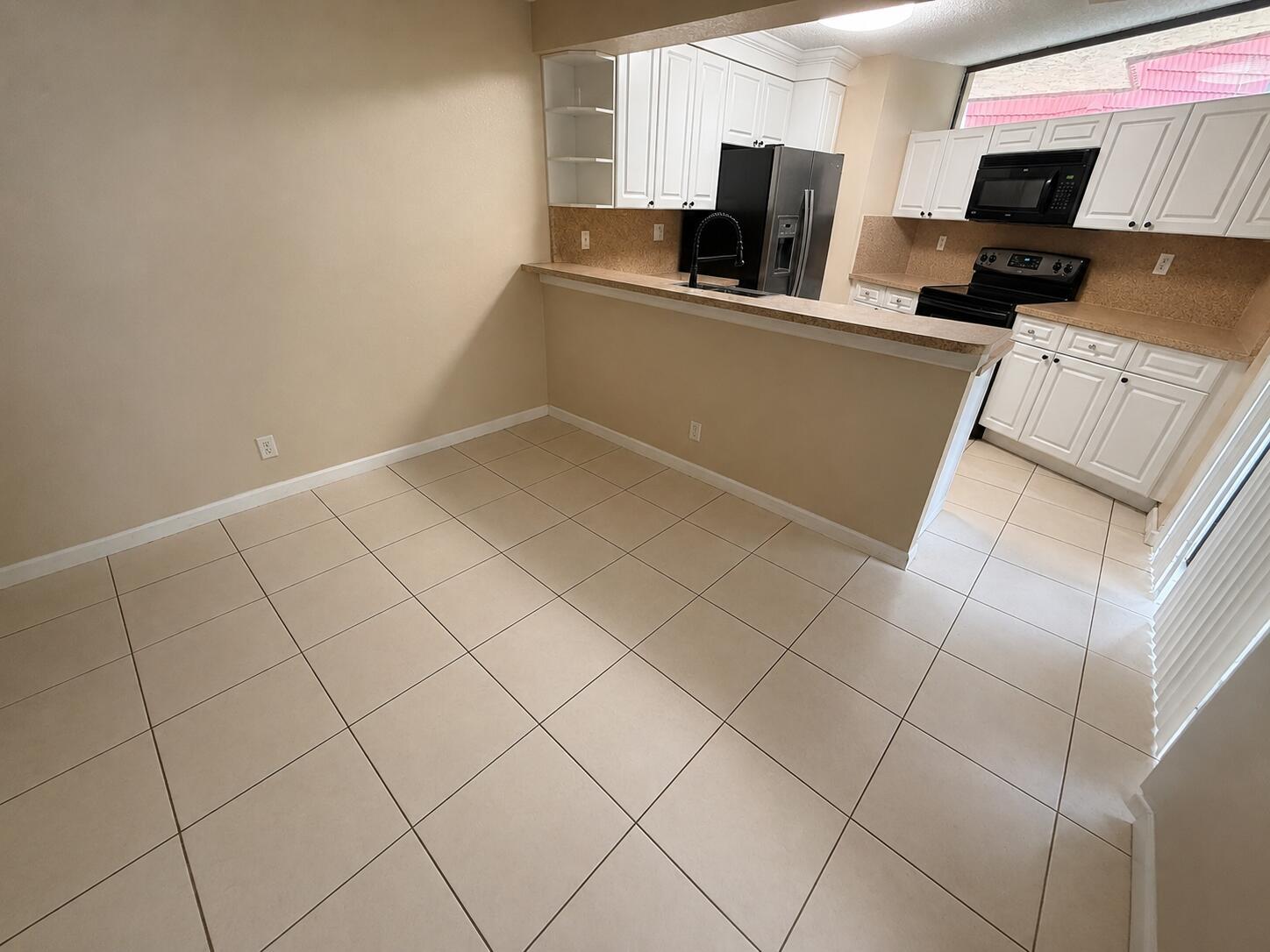 A dining area with tiled floors opens to a kitchen featuring white cabinets and appliances — 8255 Severn Drive # D, Boca Raton FL 33433, BOCA RATON, FL