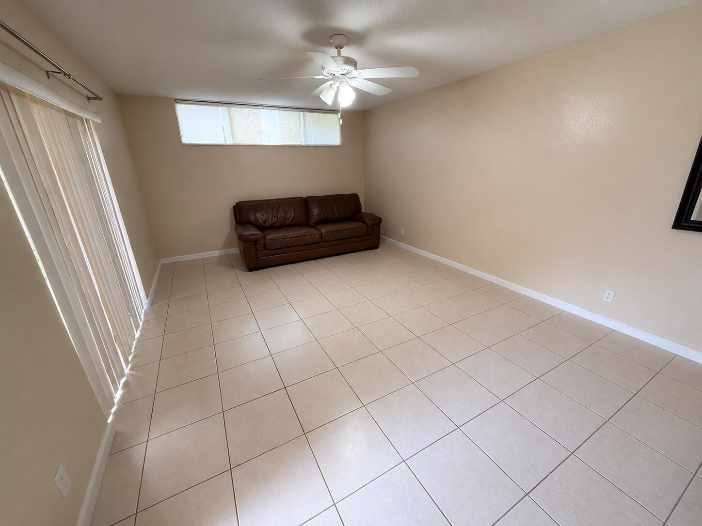A living room features beige tile flooring, a brown leather sofa, and a ceiling fan — 8255 Severn Drive # D, Boca Raton FL 33433, BOCA RATON, FL