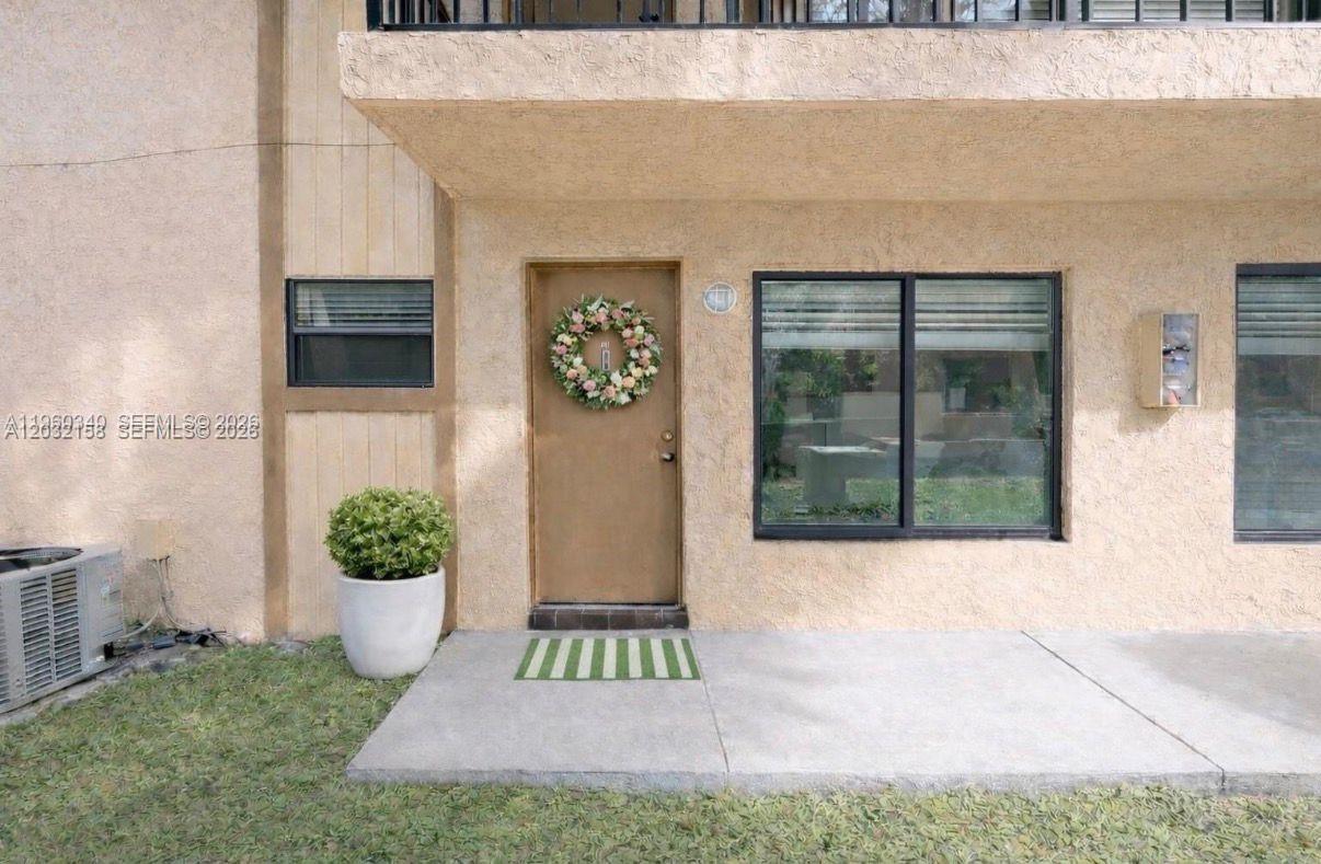 The exterior of a residential unit features a beige stucco wall, a front door with a wreath, and a concrete patio — 2530 W 67th Pl # 29, Hialeah FL 33016, HIALEAH, FL