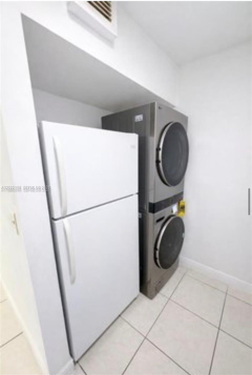 A white refrigerator stands next to a stacked washer and dryer in a tiled room — 2530 W 67th Pl # 29, Hialeah FL 33016, HIALEAH, FL