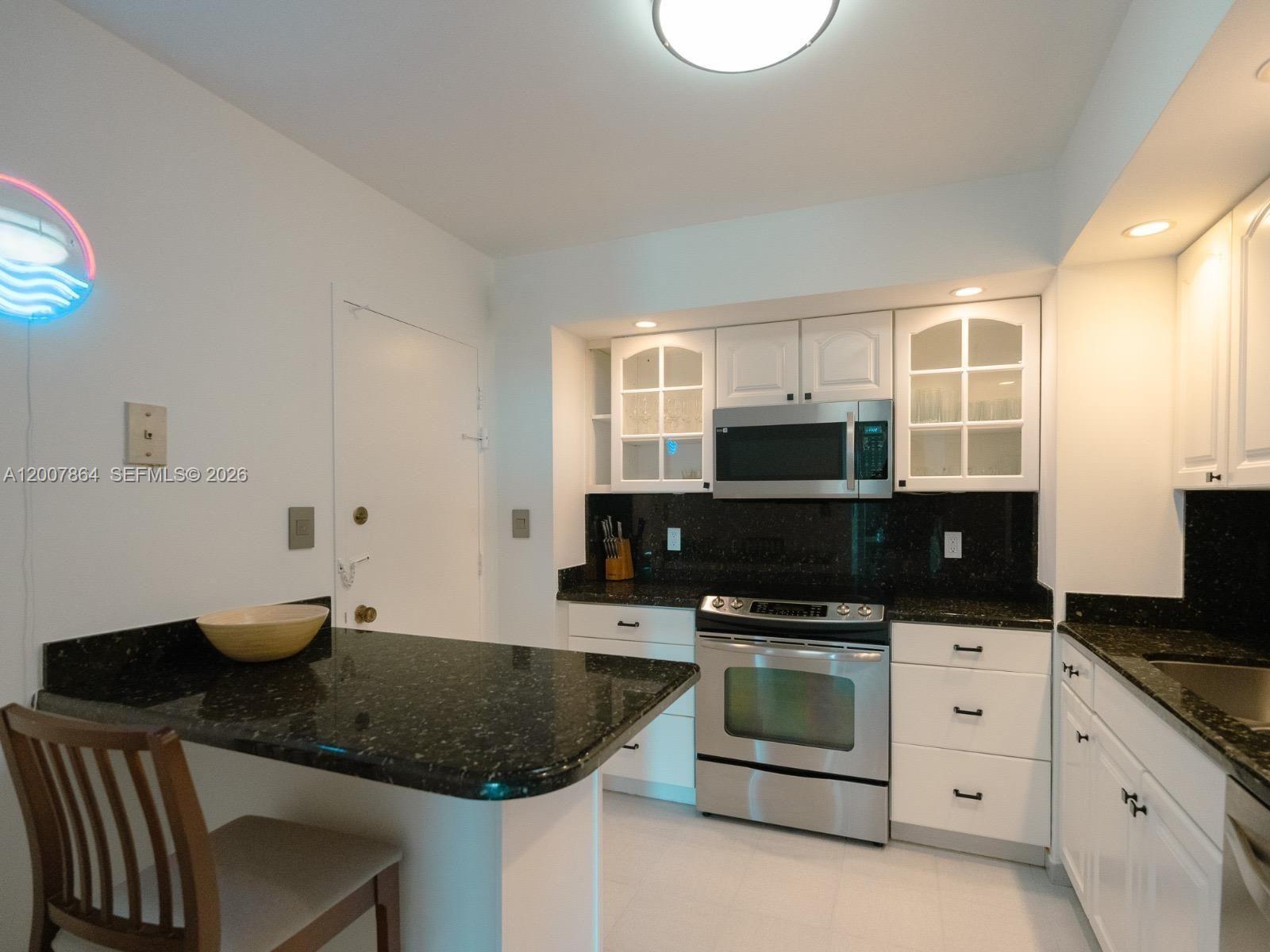 A kitchen features white cabinets, stainless steel appliances, and a black granite countertop breakfast bar — 9225 Collins Ave # 812, Surfside FL 33154, SURFSIDE, FL