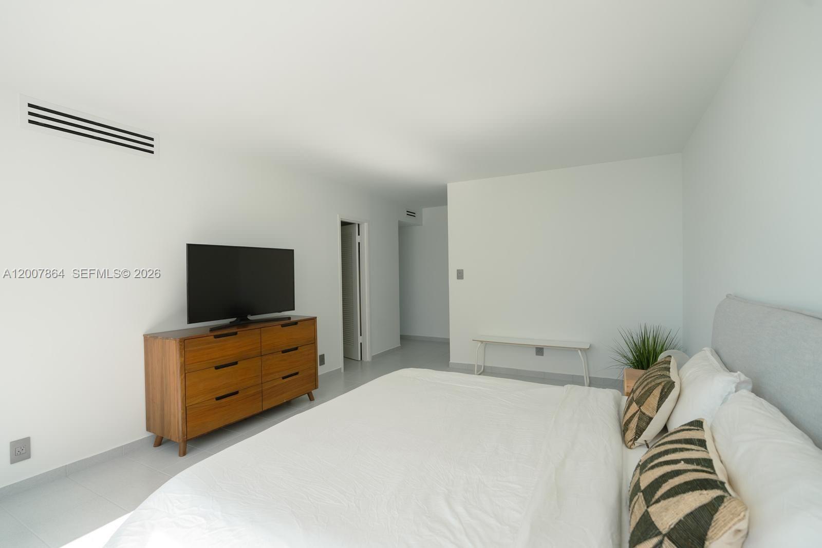 A bedroom features a wooden dresser with a television, a bed, and white walls — 9225 Collins Ave # 812, Surfside FL 33154, SURFSIDE, FL