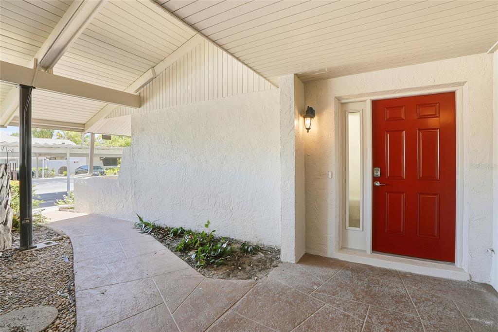 A red front door with a side window sits under a covered entryway with pavers — 1208 14TH CIRCLE SE, LARGO, FL
