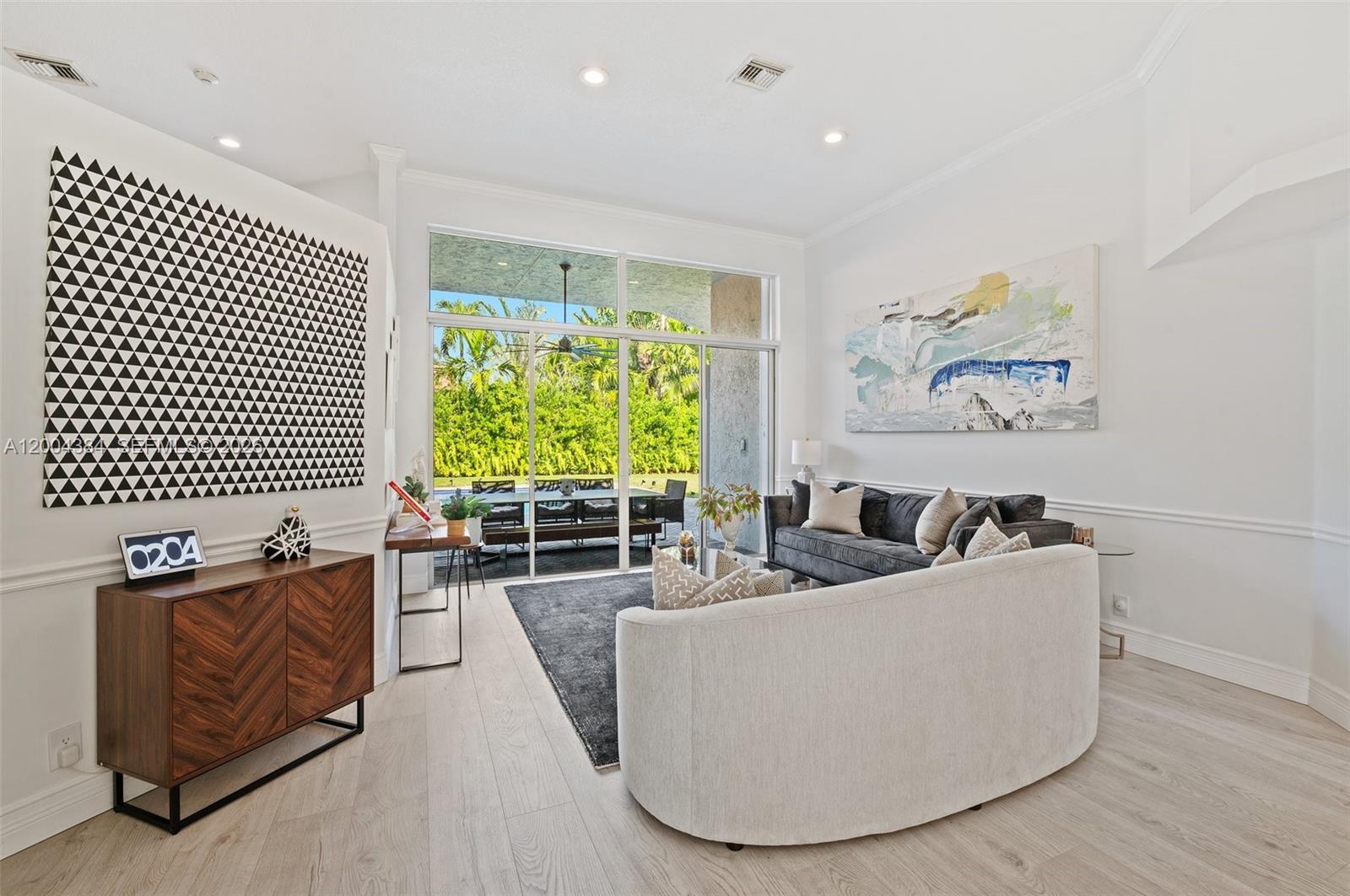 A living room features a curved sofa, dark wood cabinet, and large glass sliding doors — 765 Bayside Ln, Weston FL 33326, WESTON, FL