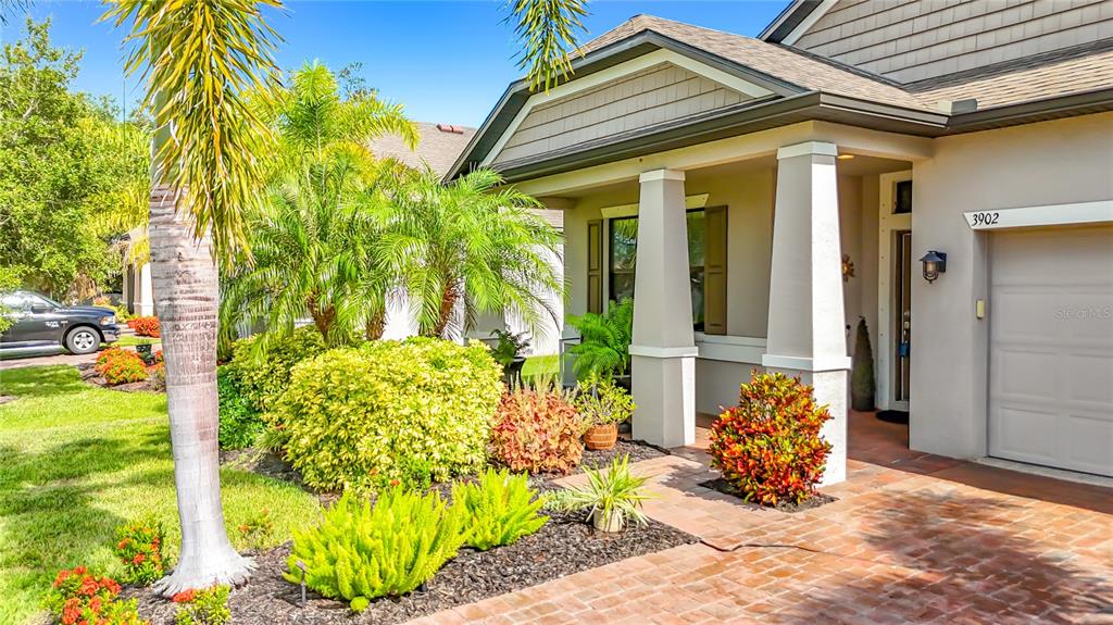 A house exterior features a brick walkway, a covered porch with columns, and landscaped bushes — 3902 76TH STREET E, PALMETTO, FL