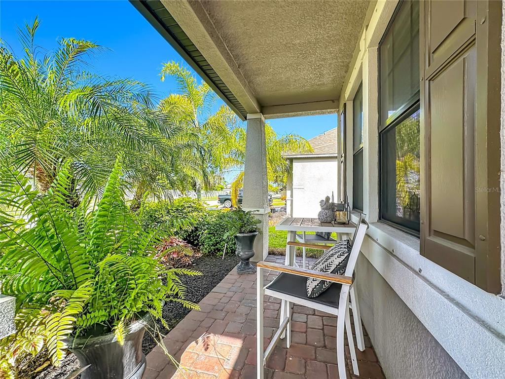 A covered brick porch features a small table, two chairs, and potted plants — 3902 76TH STREET E, PALMETTO, FL