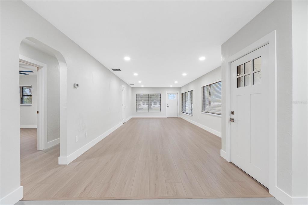 A bright, empty living room features light wood-look flooring, white walls, and recessed lighting — 1005 APACHE TRAIL, CLEARWATER, FL