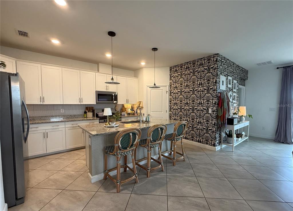 A kitchen features white cabinetry, granite countertops, a central island with barstools, and patterned wallpaper — 5132 CORAL REEF WAY, BRADENTON, FL