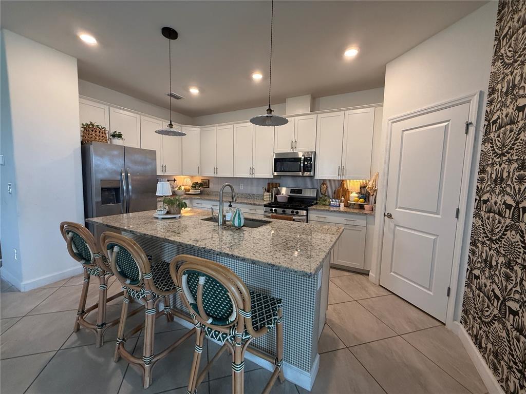 A kitchen with white cabinets, granite countertops, a central island, and three rattan bar stools — 5132 CORAL REEF WAY, BRADENTON, FL