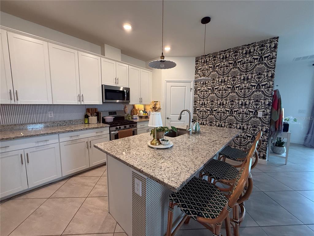 A kitchen features white cabinets, granite countertops, a central island with bar stools, and patterned wallpaper — 5132 CORAL REEF WAY, BRADENTON, FL