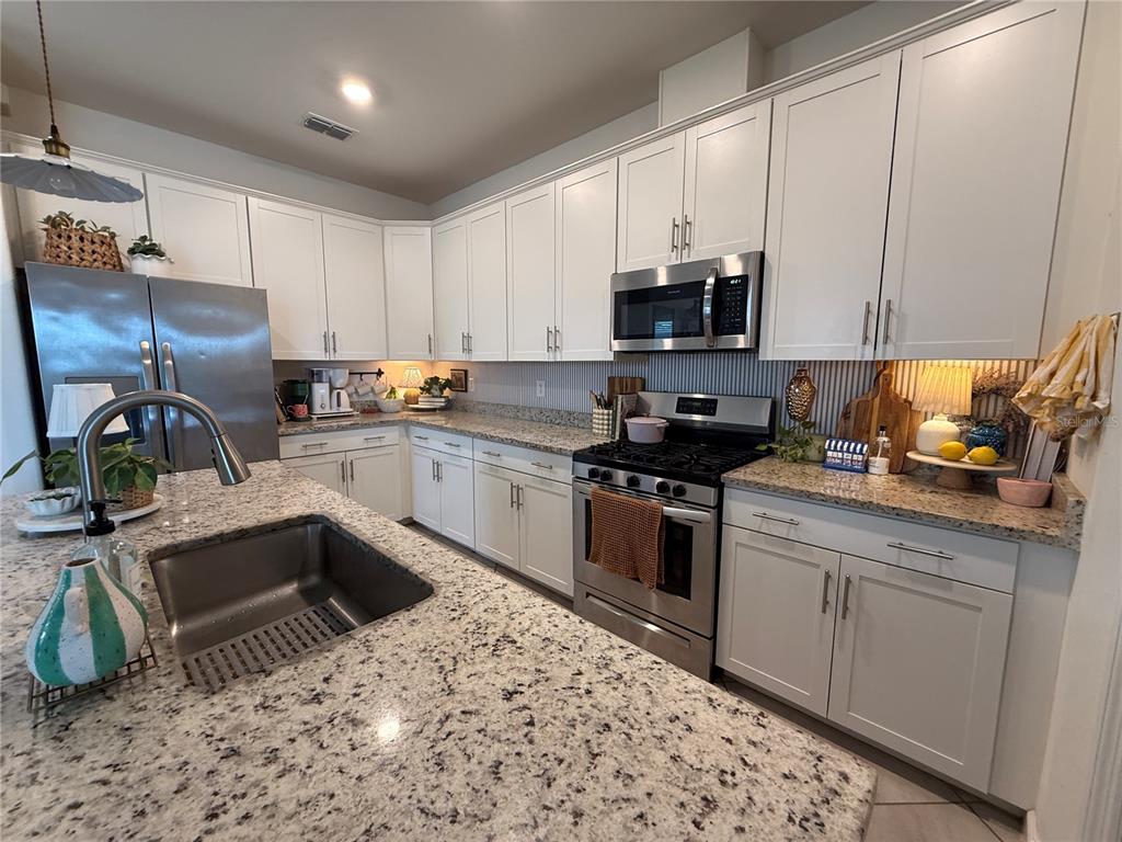 A kitchen features white cabinets, granite countertops, stainless steel appliances, and a large island sink — 5132 CORAL REEF WAY, BRADENTON, FL