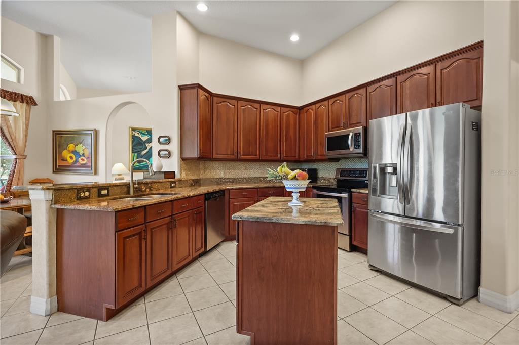 A kitchen features wood cabinets, granite countertops, stainless steel appliances, and a central island — 4332 FAWN MEADOWS CIRCLE, CLERMONT, FL