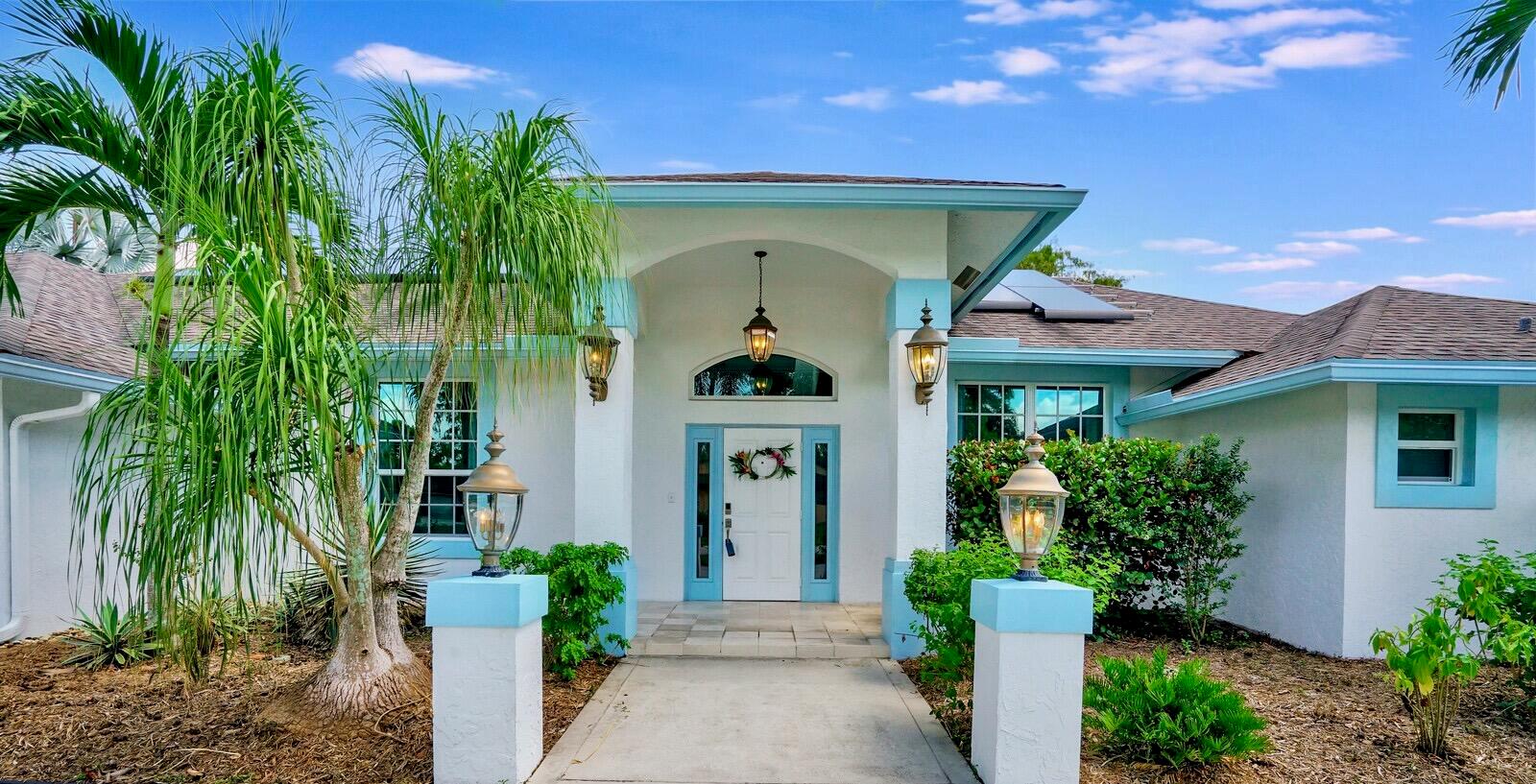 The exterior of a white house with blue trim features a palm tree and walkway — 1212 Mulberry Place, Wellington FL 33414, WELLINGTON, FL