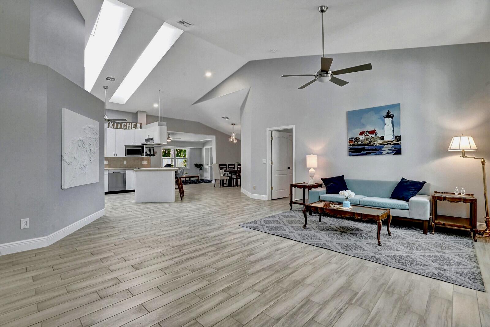 An open-concept living area features vaulted ceilings, light wood-look tile flooring, and a modern kitchen — 1212 Mulberry Place, Wellington FL 33414, WELLINGTON, FL