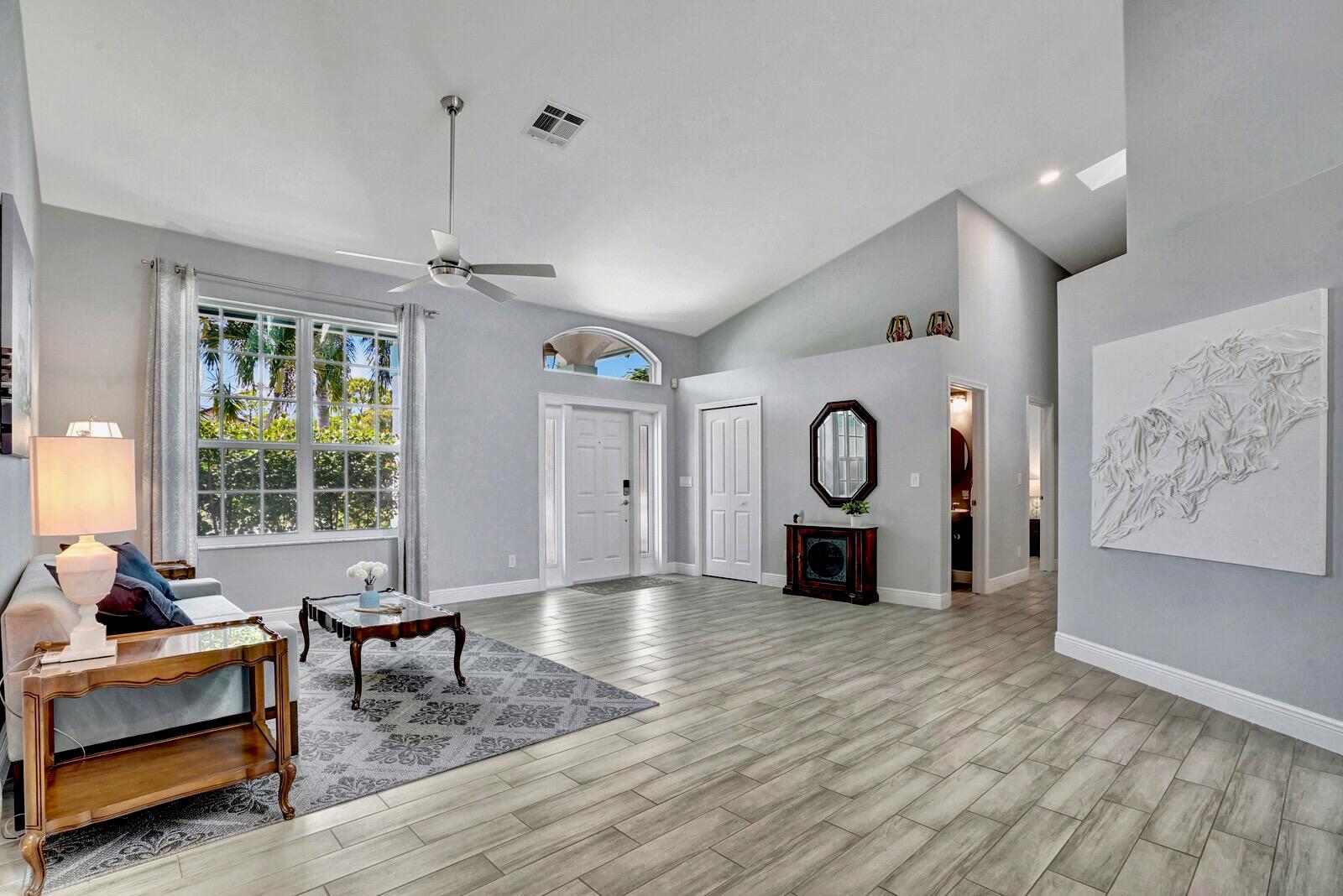 A living room with light gray walls, wood-look tile flooring, and a vaulted ceiling — 1212 Mulberry Place, Wellington FL 33414, WELLINGTON, FL