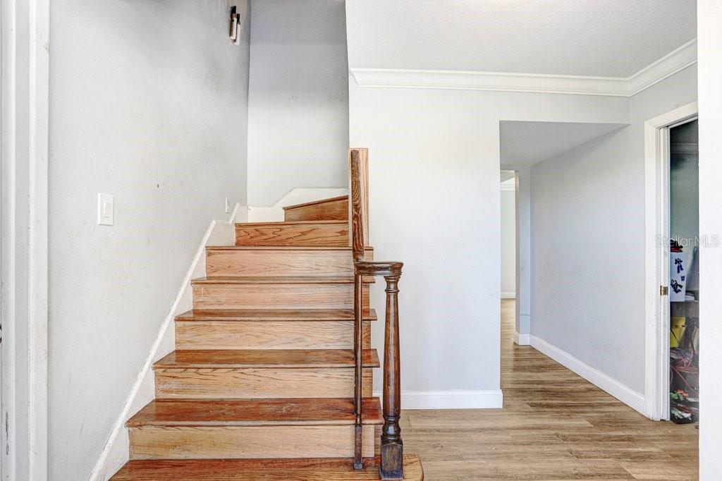 A wooden staircase with a dark railing leads upward next to a hallway with flooring — 17308 TOBACCO ROAD, LUTZ, FL