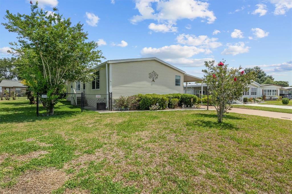 A light-colored manufactured home sits on a grassy lot with a chain-link fence — 1610 REYNOLDS ROAD Lot 32, LAKELAND, FL