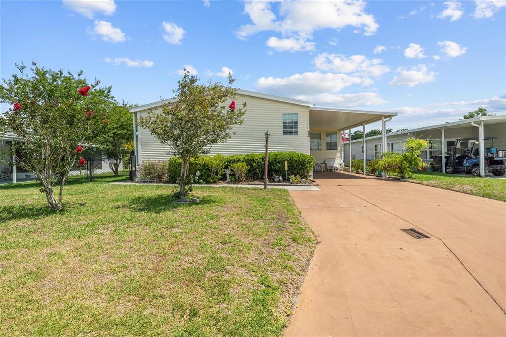 A single-story manufactured home with a tan exterior, a carport, and a paved driveway — 1610 REYNOLDS ROAD Lot 32, LAKELAND, FL