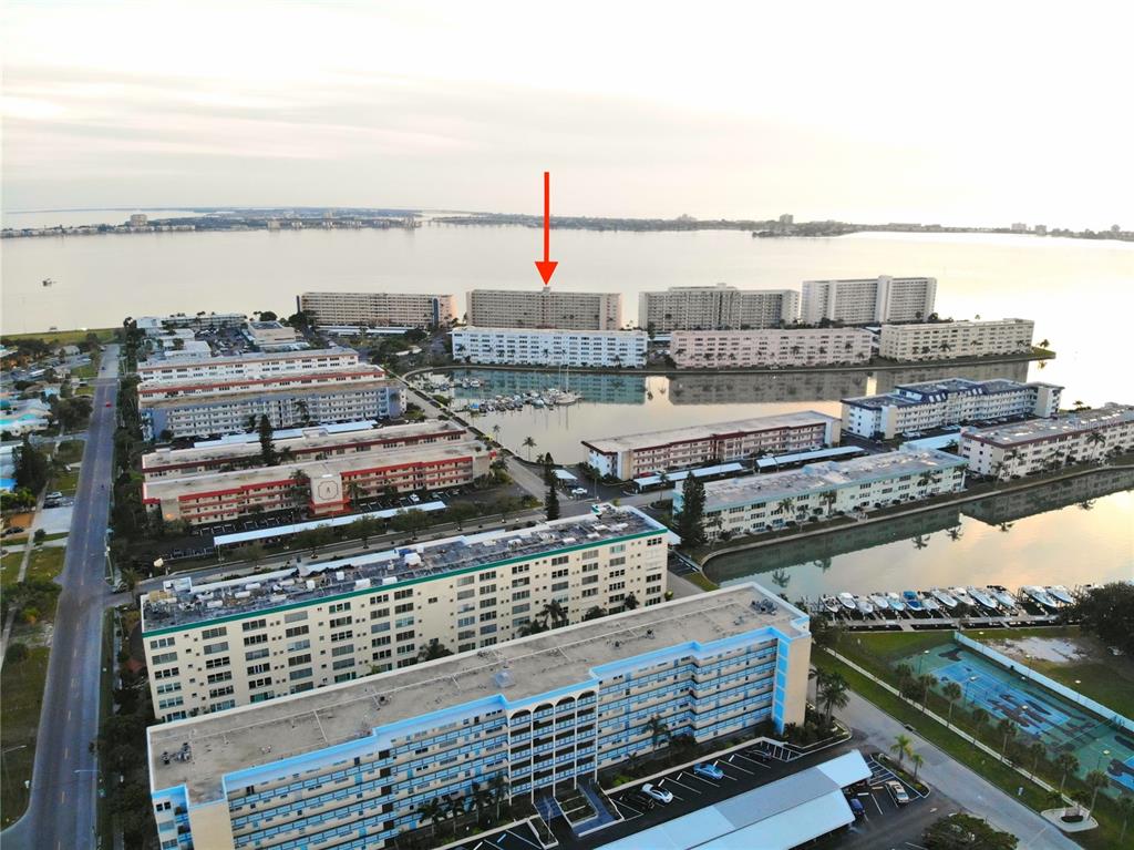 An aerial view shows multiple multi-story apartment buildings surrounding a marina and a large bay — 5980 SHORE BOULEVARD S UNIT 405, GULFPORT, FL