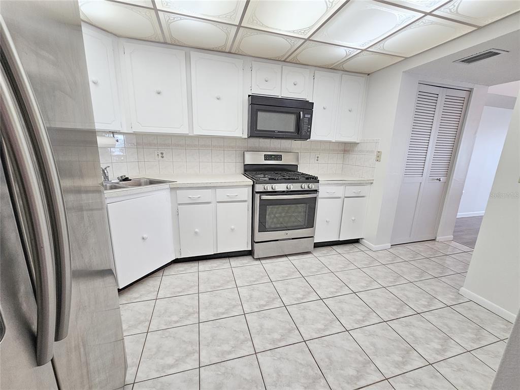 A kitchen features white cabinets, stainless steel appliances, a tiled backsplash, and light-colored floor tiles — 5980 SHORE BOULEVARD S UNIT 405, GULFPORT, FL