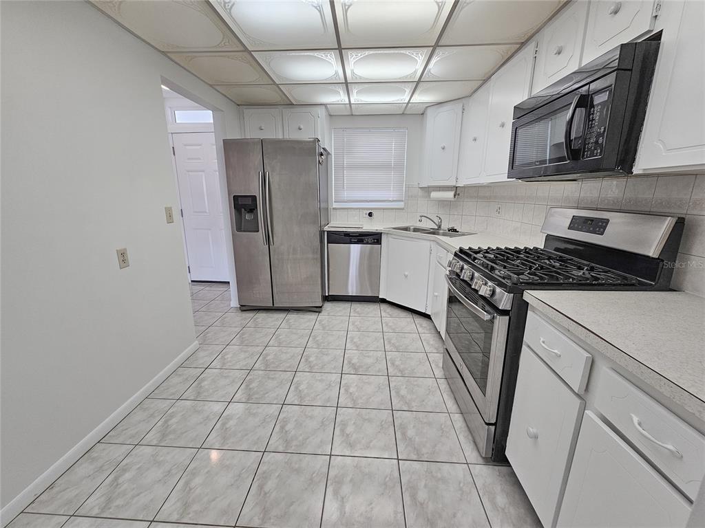 A kitchen features white cabinets, stainless steel appliances, tiled floors, and a drop ceiling — 5980 SHORE BOULEVARD S UNIT 405, GULFPORT, FL
