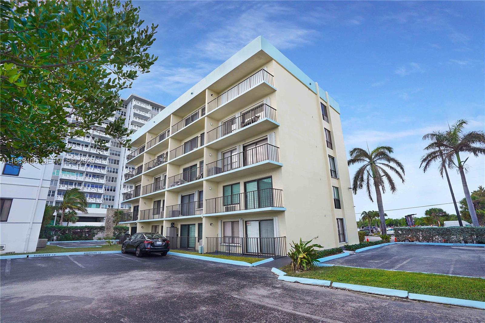 A multi-story apartment building with balconies stands next to a parking lot with palm trees — 3215 N Ocean Dr # 301, Hollywood FL 33019, HOLLYWOOD, FL