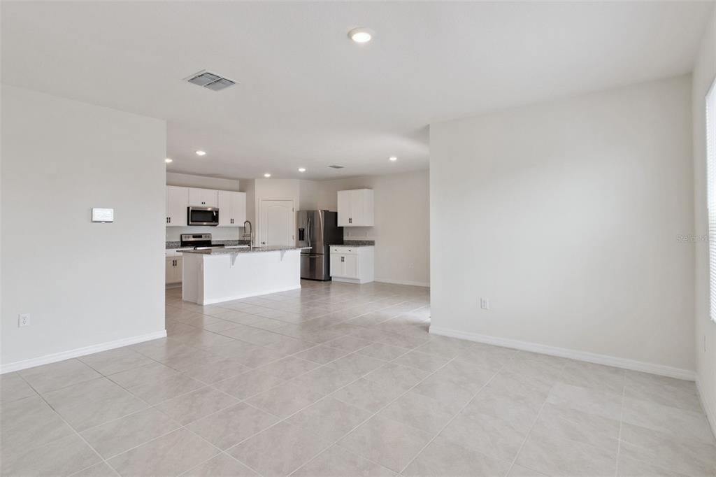 An open-concept kitchen with white cabinetry and stainless steel appliances overlooks a tiled living area — 4373 DELEON STREET, HAINES CITY, FL