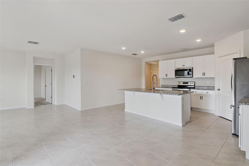 A kitchen with white cabinets, granite countertops, and a center island opens to a room — 4373 DELEON STREET, HAINES CITY, FL