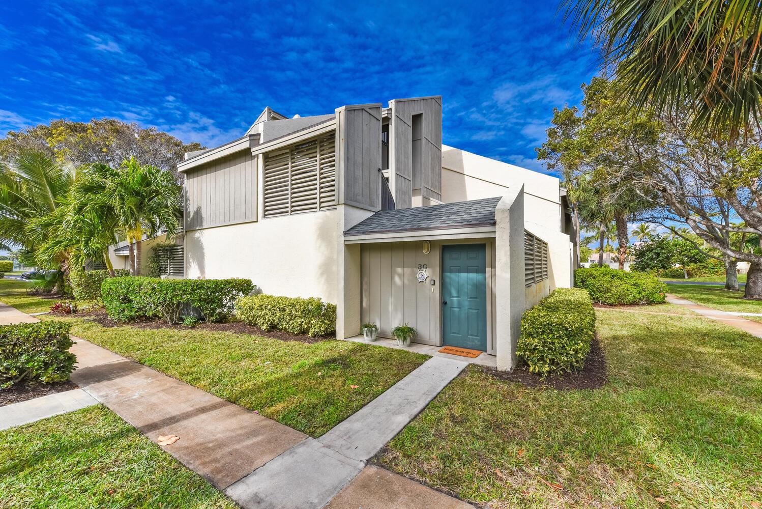 A two-story townhouse with a teal front door, beige siding, and surrounding tropical landscaping — 1605 S Us Highway 1, Jupiter FL 33477, JUPITER, FL