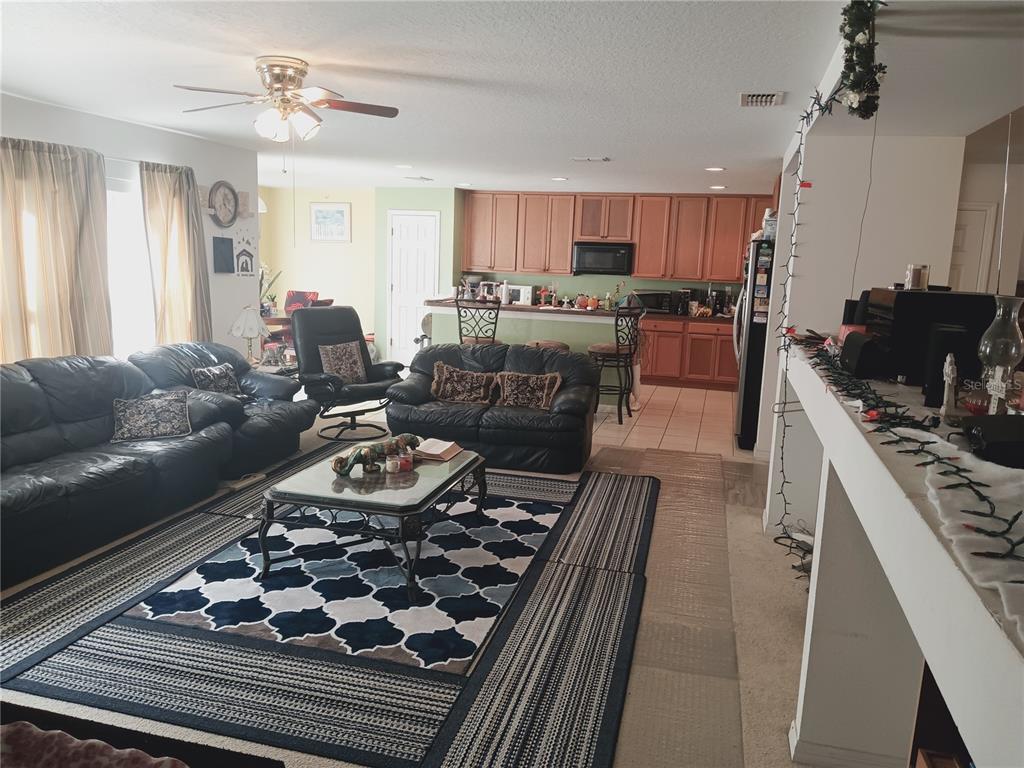 A living room with leather furniture and a patterned rug opens to a kitchen area — 2474 MALLOW OAK COURT, APOPKA, FL