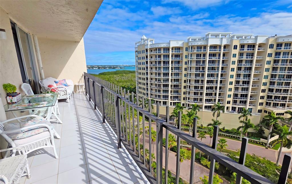 A balcony with patio furniture overlooks a large apartment complex and a distant body of water — 1212 BEN FRANKLIN DRIVE UNIT 1205, SARASOTA, FL