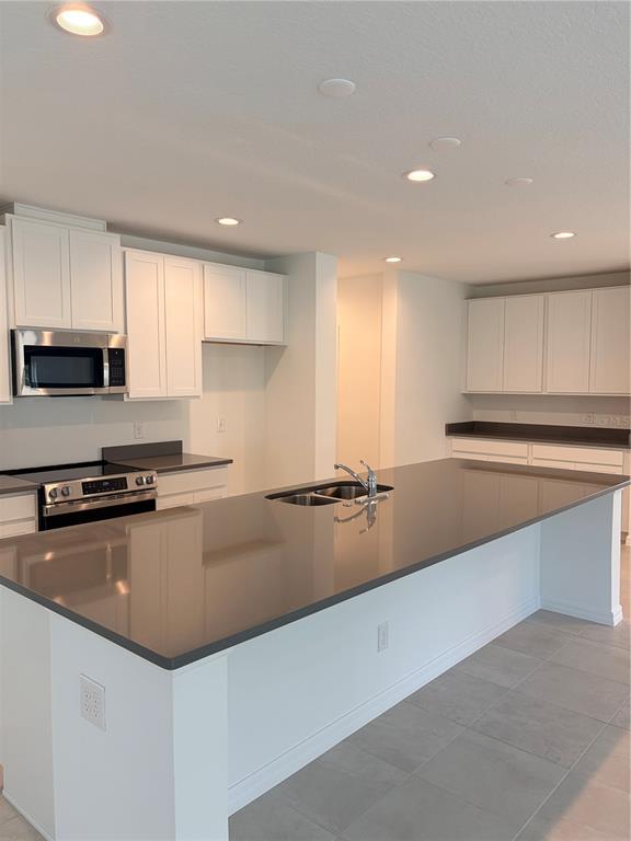A modern kitchen features white cabinetry, a large gray island countertop, and stainless steel appliances — 1349 SAWGRASS HAMMOCK LANE, DAVENPORT, FL