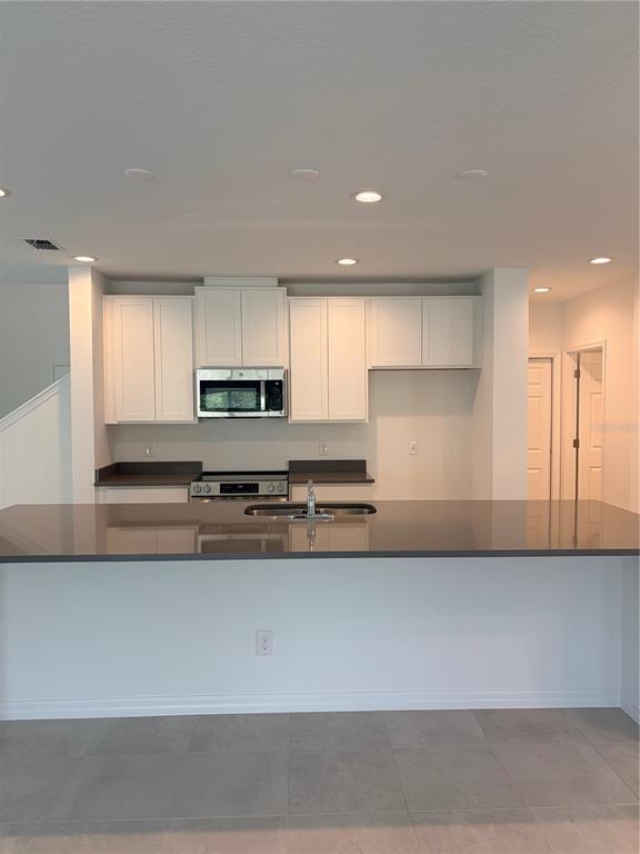 A kitchen features white cabinets, dark countertops, a stainless steel microwave, and a center island — 1349 SAWGRASS HAMMOCK LANE, DAVENPORT, FL
