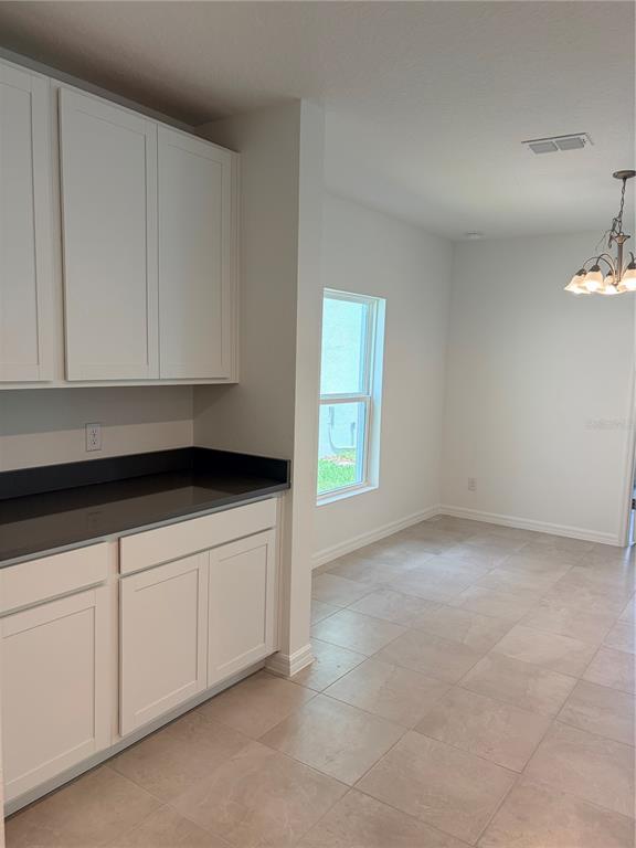 A kitchen area features white cabinets, dark countertops, and tile flooring next to a dining space — 1349 SAWGRASS HAMMOCK LANE, DAVENPORT, FL