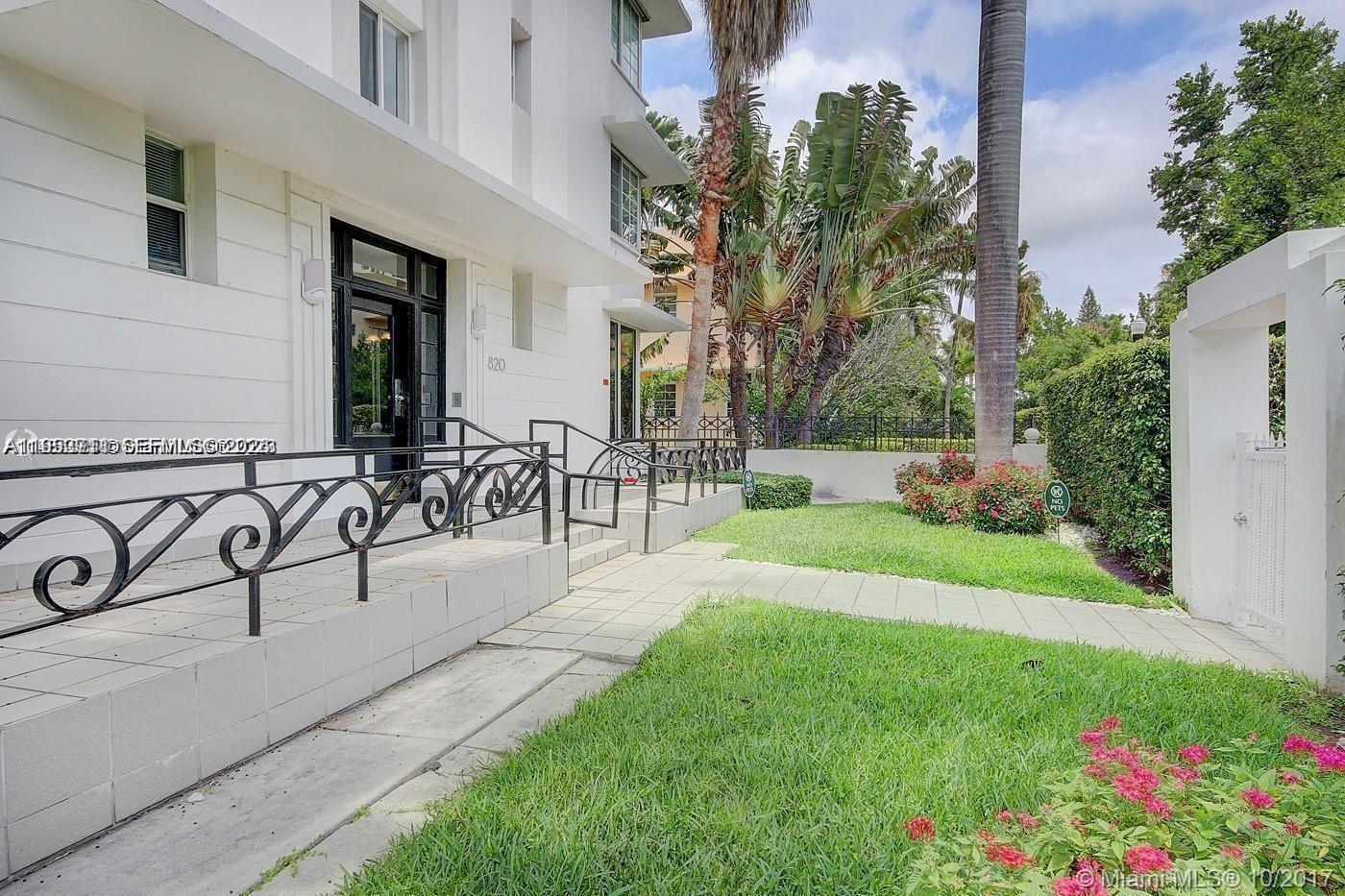 A white building exterior features a paved walkway, black metal railings, and landscaped green space — 820 Euclid Ave # 106, Miami Beach FL 33139, MIAMI BEACH, FL