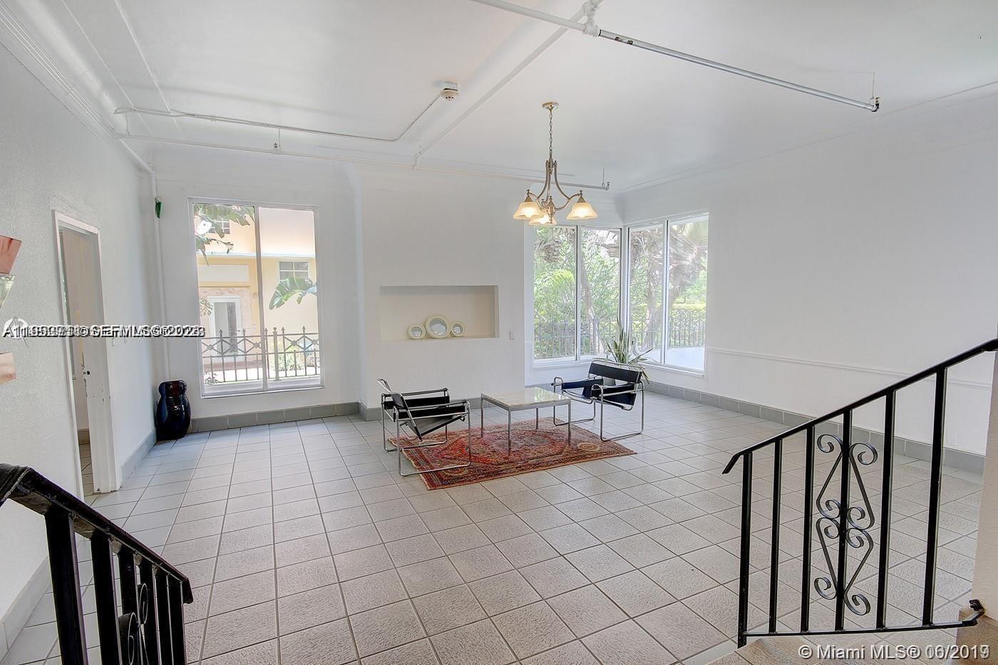 A bright living room features white walls, tiled floors, a chandelier, and a staircase — 820 Euclid Ave # 106, Miami Beach FL 33139, MIAMI BEACH, FL