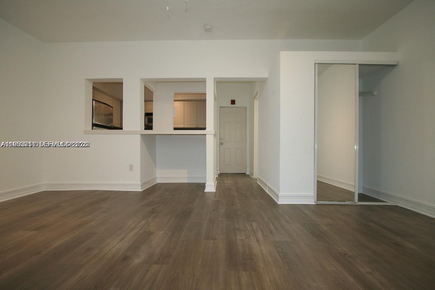 A room with wood-look flooring, a kitchen pass-through window, and a mirrored closet door — 820 Euclid Ave # 106, Miami Beach FL 33139, MIAMI BEACH, FL