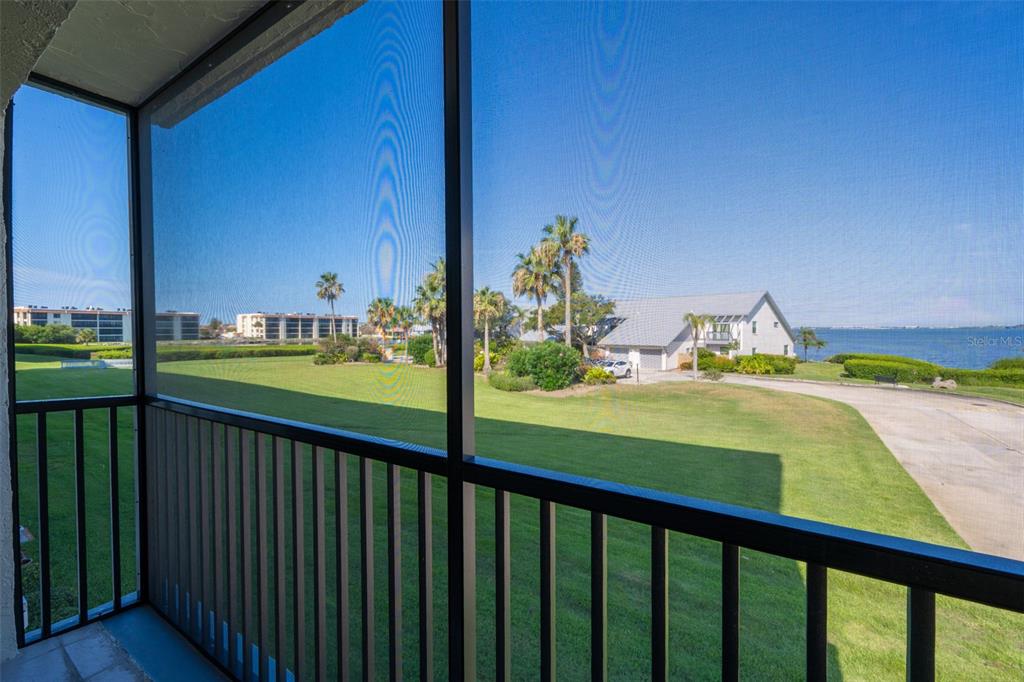 A screened-in balcony overlooks a grassy lawn, palm trees, a house, and a body of water — 3165 N ATLANTIC AVENUE UNIT B209, COCOA BEACH, FL