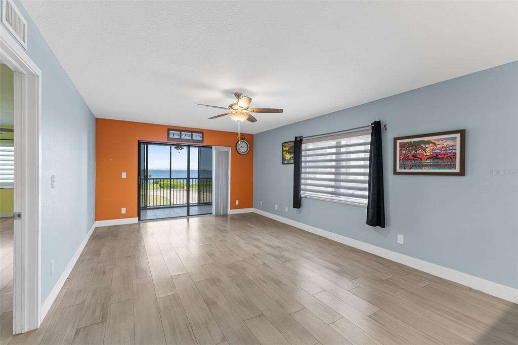 A living room with light blue and orange walls, wood-look flooring, and a sliding glass door — 3165 N ATLANTIC AVENUE UNIT B209, COCOA BEACH, FL