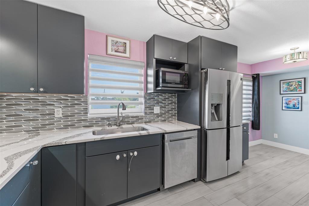 A kitchen features dark grey cabinets, a patterned tile backsplash, and stainless steel appliances — 3165 N ATLANTIC AVENUE UNIT B209, COCOA BEACH, FL