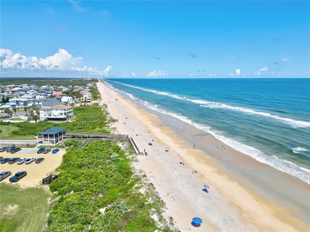 An aerial view shows a sandy beach, ocean waves, a parking lot, and coastal homes — 3 BAY DRIVE, PALM COAST, FL