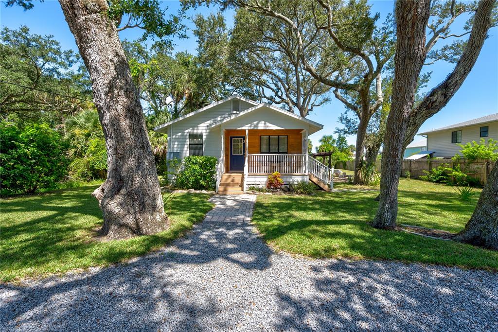 A white cottage with a covered front porch sits behind a gravel driveway and trees — 3 BAY DRIVE, PALM COAST, FL